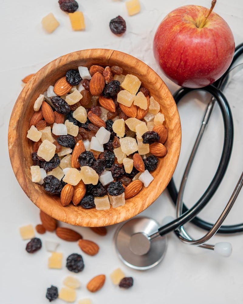 Top view of a healthy mix of nuts and dried fruits with an apple and stethoscope.