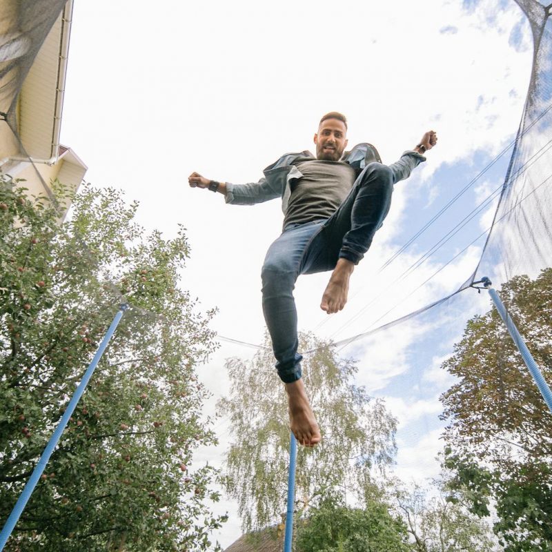 Photo by Yan Krukau Energetic man in midair on trampoline, surrounded by trees and clear sky.