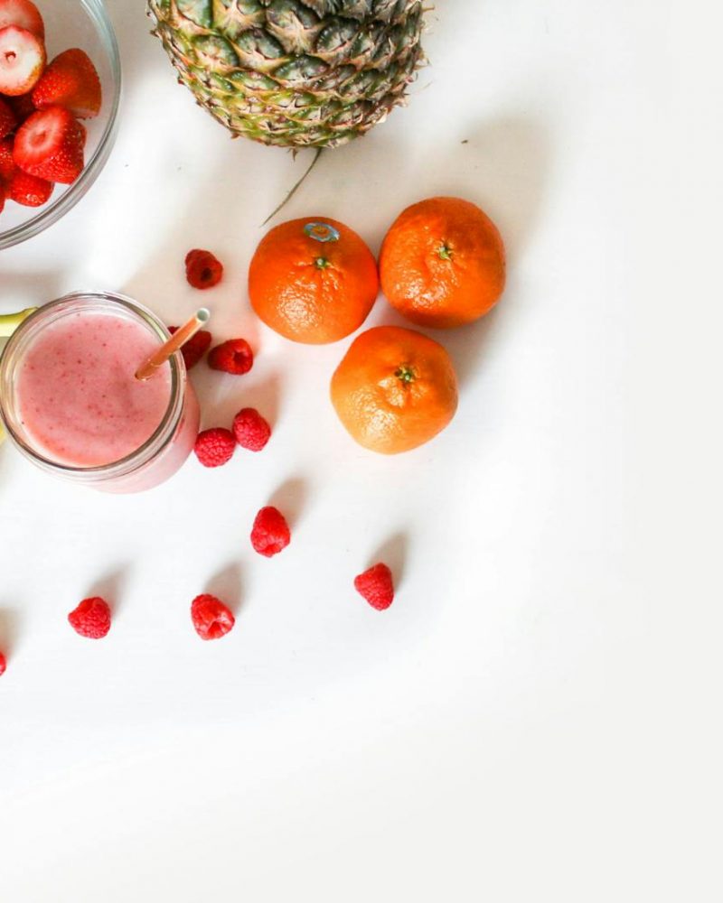 A vibrant flat lay of tropical fruits including bananas, strawberries, and a smoothie on a white background.